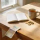 Tidy Australian kitchen table with an open notebook, a cup of tea, gold coins and a five dollar note in soft morning light