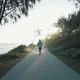 Runner seen from behind on a wide empty coastal path in Australia on a crisp winter morning, wearing light layers, with low coastal scrub and pale ocean beside the path