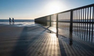 Empty Australian beach on a crisp winter morning with a low bright sun over the water and long shadows across damp sand, a couple walking in the distance in light jackets