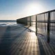 Empty Australian beach on a crisp winter morning with a low bright sun over the water and long shadows across damp sand, a couple walking in the distance in light jackets