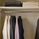 Neat rail of winter clothes in a muted palette of cream, charcoal and navy in a tidy Australian bedroom wardrobe, folded knitwear on a shelf above