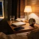 A bedside table in an ordinary Australian home late at night lit by one small warm lamp and a sliver of light from a hallway, with a half-drunk glass of water, a folded tea towel, a small plain clock, a closed book with a blank cover and a phone lying dark beside rumpled bedding with the dark street beyond the curtain
