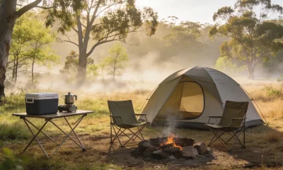 Simple dome tent at a small Australian spring campsite in early morning light, with two camp chairs by a fire ring, an esky and a camp stove on a folding table, eucalyptus trees behind.