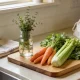 organised Australian kitchen bench with fresh vegetables, herbs in water and a folded tea towel in soft morning light