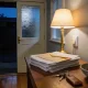 The front entry of an ordinary Australian house in the evening, with a table lamp lit above a stack of plain mail topped by a sealed envelope, a set of keys with a leather fob and a ceramic bowl of coins on a timber hall table, a jacket on a wall hook and an open front door with a frosted panel looking onto a dark porch, over polished floorboards
