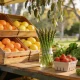 Spring fruit and vegetables piled on a wooden market stall at an Australian farmers market, with citrus crates, asparagus standing in water and a punnet of strawberries